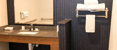 A bathroom with a wooden vanity, a large mirror, and a towel rack with towels.