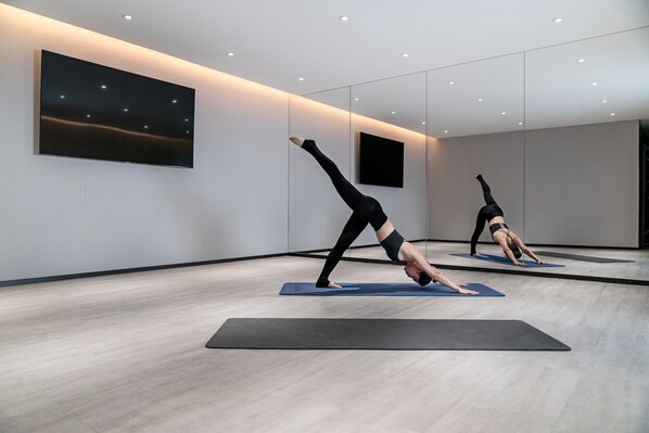 Un studio de yoga moderne avec des murs recouverts de miroirs, un grand téléviseur à écran plat et un plancher en bois.