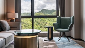 A modern hotel room with a sofa, a round table, a chair, and a view of a green landscape through large windows. - The G Shenzhen, A Tribute Portfolio Hotel (Shenzhen)