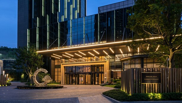 A modern building with a glass facade, a large entrance with a metal sculpture, and a well-lit pathway. - The G Shenzhen, A Tribute Portfolio Hotel (Shenzhen)