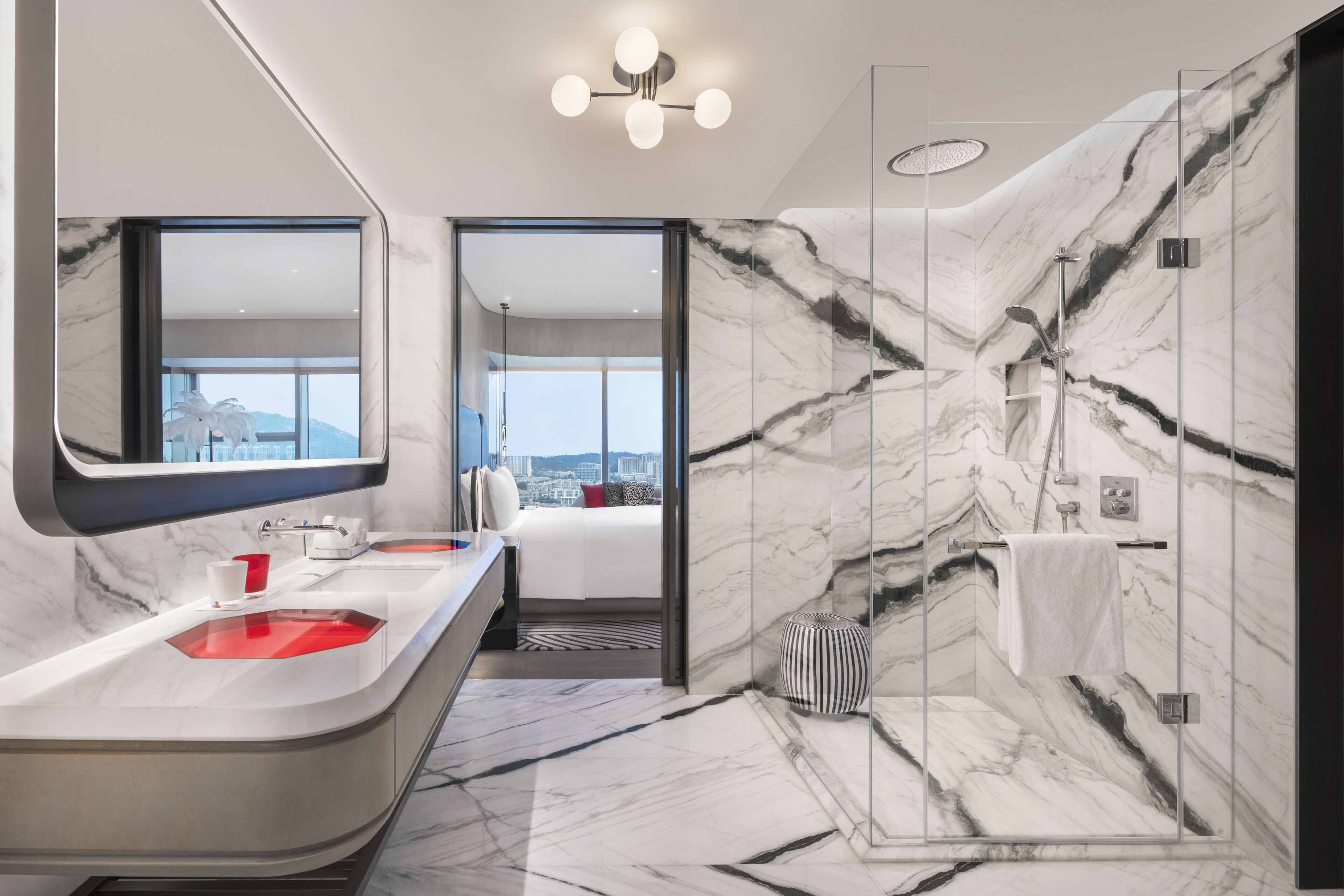 A modern bathroom with a marble vanity, a shower with a glass enclosure, and a view of a cityscape through an open door.