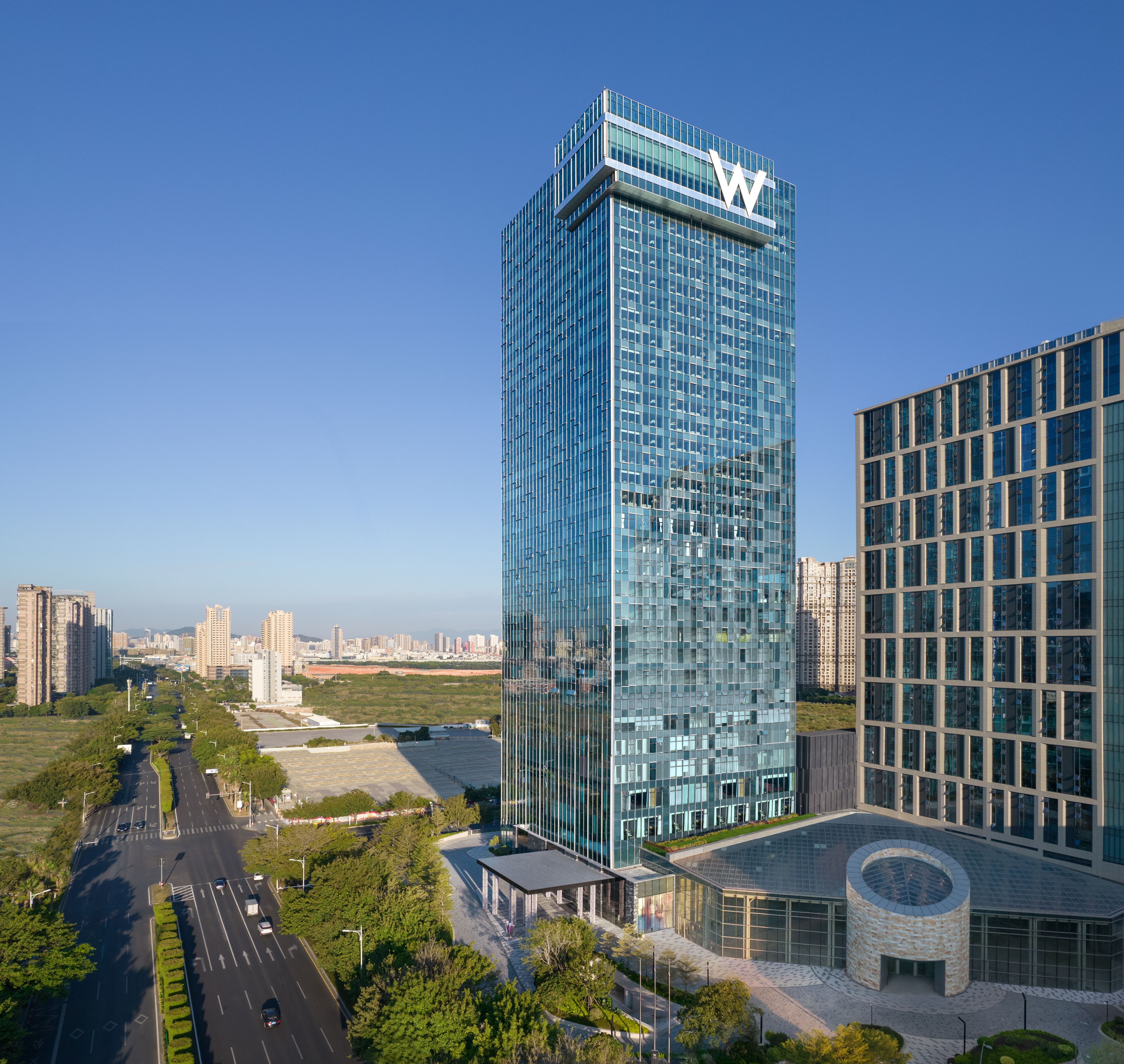 A modern high-rise building with a prominent 'W' logo, surrounded by other high-rise buildings and a clear sky.