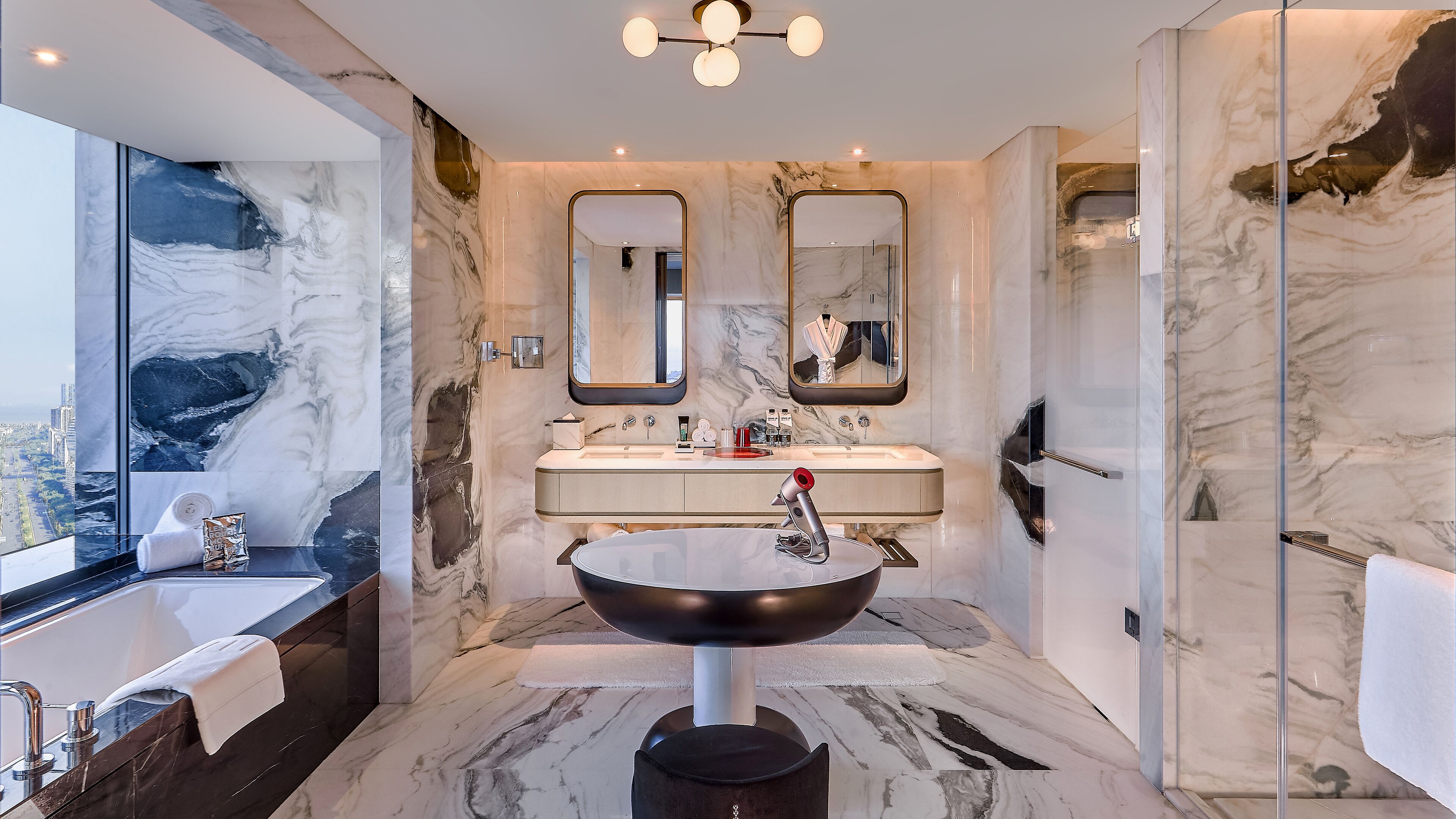 A modern bathroom with a large marble sink, two mirrors, and a glass shower enclosure.