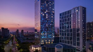 A modern high-rise building with a prominent 'W' logo at the top, surrounded by other high-rise buildings and a busy street below. - W Xiamen (Xiamen)