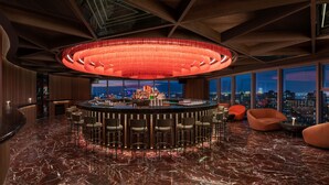 A modern bar area with a circular bar, multiple stools, and a large chandelier. - W Xiamen (Xiamen)