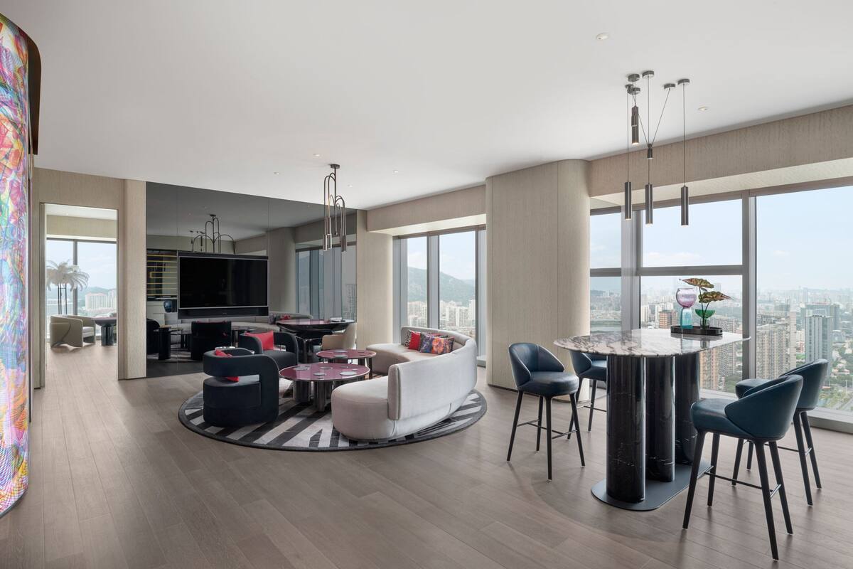 A spacious living area with a round dining table, modern seating, and large windows offering a city view.