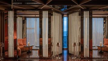 Un lobby lujoso con techos altos, columnas reflectantes y zonas de descanso con sofás cómodos y mesas.