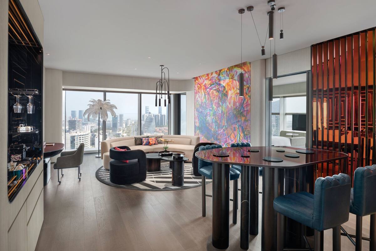 A modern living room with a large window, a round dining table, and a colorful abstract painting.