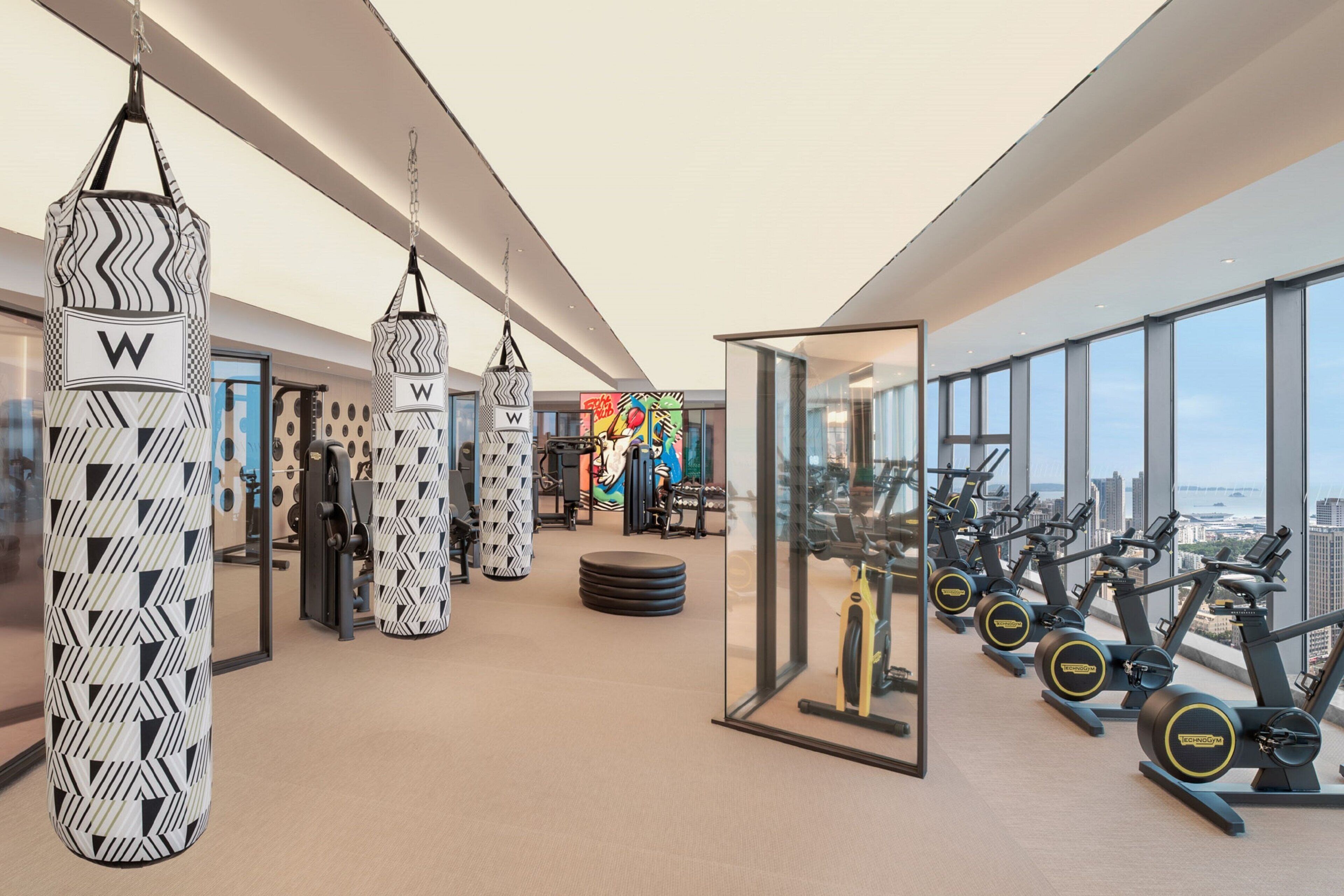 A modern gym with punching bags, exercise equipment, and a city view.