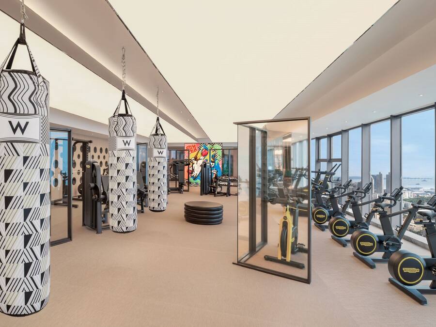 A modern gym with punching bags, exercise equipment, and a city view.