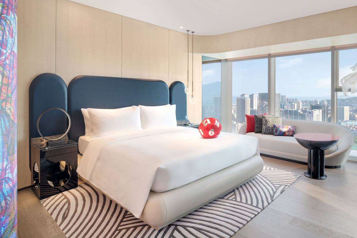 A modern hotel room with a large bed, a sofa, and a city view.