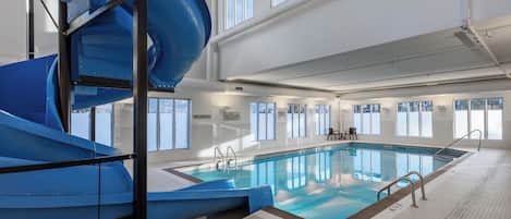 An indoor swimming pool with a blue slide, large windows, and a no diving sign.