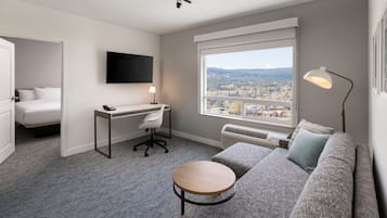 Een moderne hotelkamer met een groot raam, een grijze bank, een ronde tafel, een bureau met stoel en een bed.