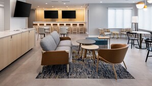 A modern hotel lobby with a sofa, chairs, a coffee table, a TV, and a bar area. - TownePlace Suites by Marriott West Kelowna (West Kelowna)