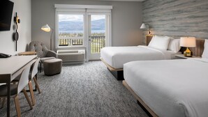 A hotel room with two beds, a desk, a chair, a balcony with a view of mountains, and a mounted TV. - TownePlace Suites by Marriott West Kelowna (West Kelowna)