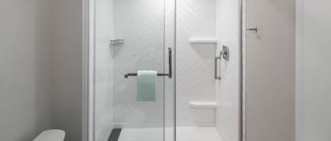 Un baño moderno con ducha de vidrio, paredes con azulejos blancos y un perchero visible.