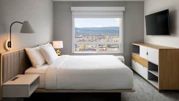 A modern hotel room with a large bed, a TV, a desk, and a window with a city view.