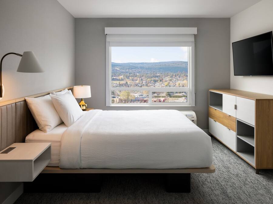 Une chambre d’hôtel moderne dotée d’un grand lit, d’une télévision, d’un bureau et d’une fenêtre donnant sur la ville.