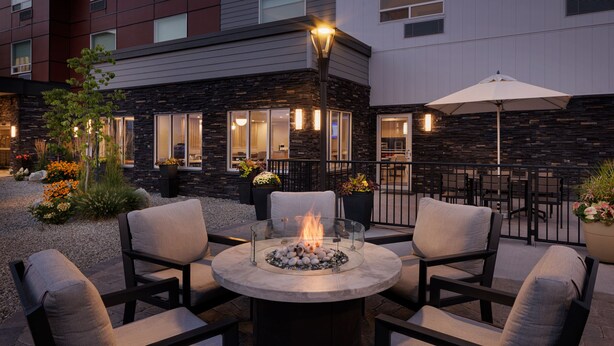 An outdoor patio with a round table, four chairs, a fire pit, and a street lamp. - TownePlace Suites by Marriott West Kelowna (West Kelowna)
