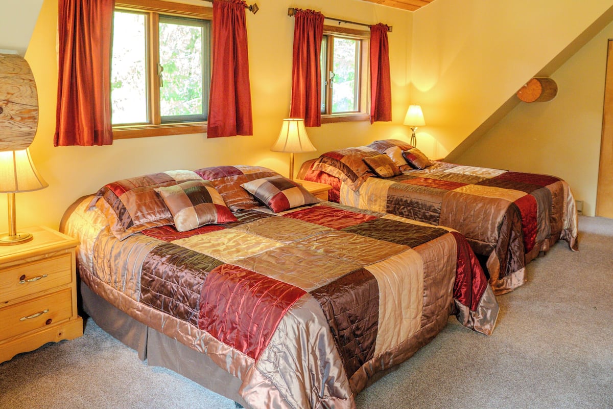A bedroom with two beds, wooden ceiling beams, and a window with curtains.