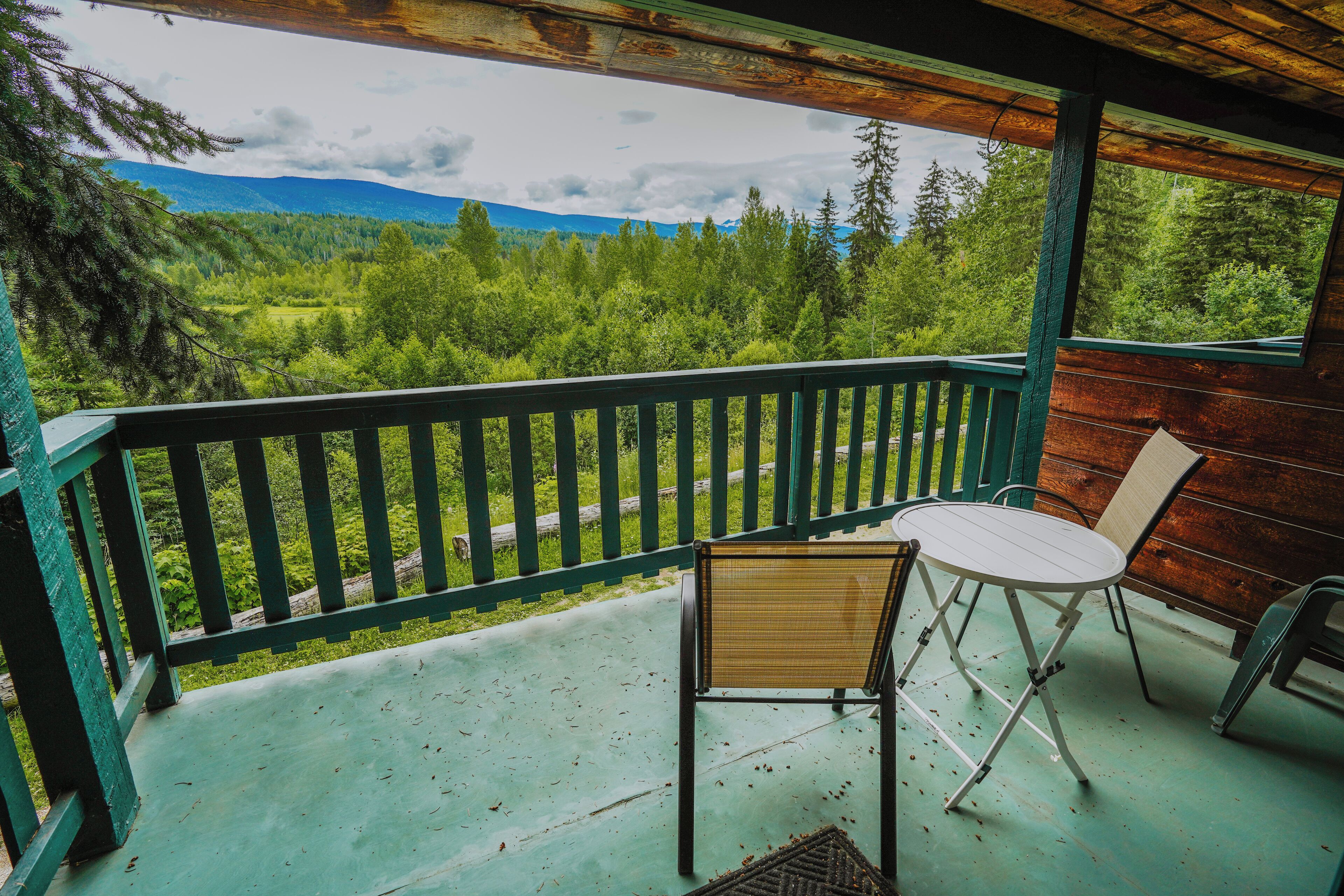 Un espace extérieur abrité offrant une vue sur une forêt et des montagnes. On y trouve deux chaises et une table.