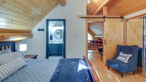 A bedroom with a bed, a chair, wooden walls, and a door leading to a bathroom. - 'The InnLet' - Comfy Cabin By Conkling Marina (Worley)