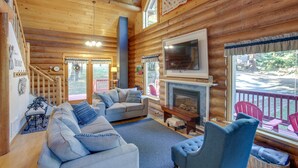 A cozy log cabin interior with a fireplace, a large TV mounted above it, and a view of the outdoor deck. - 'The InnLet' - Comfy Cabin By Conkling Marina (Worley)