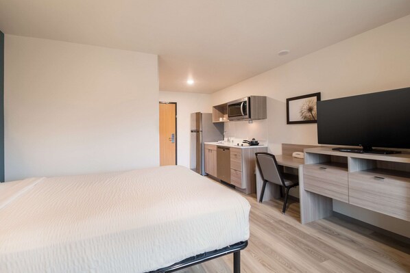 A compact room with a bed, a kitchenette, a desk, and a television.