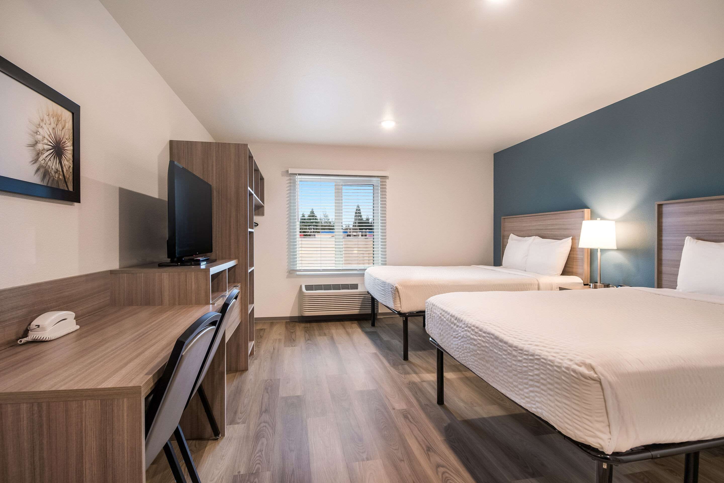 A hotel room with two beds, a desk with a telephone, a television, and a window with blinds.