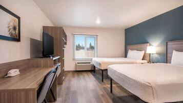 A hotel room with two beds, a desk with a telephone, a television, and a window with blinds.