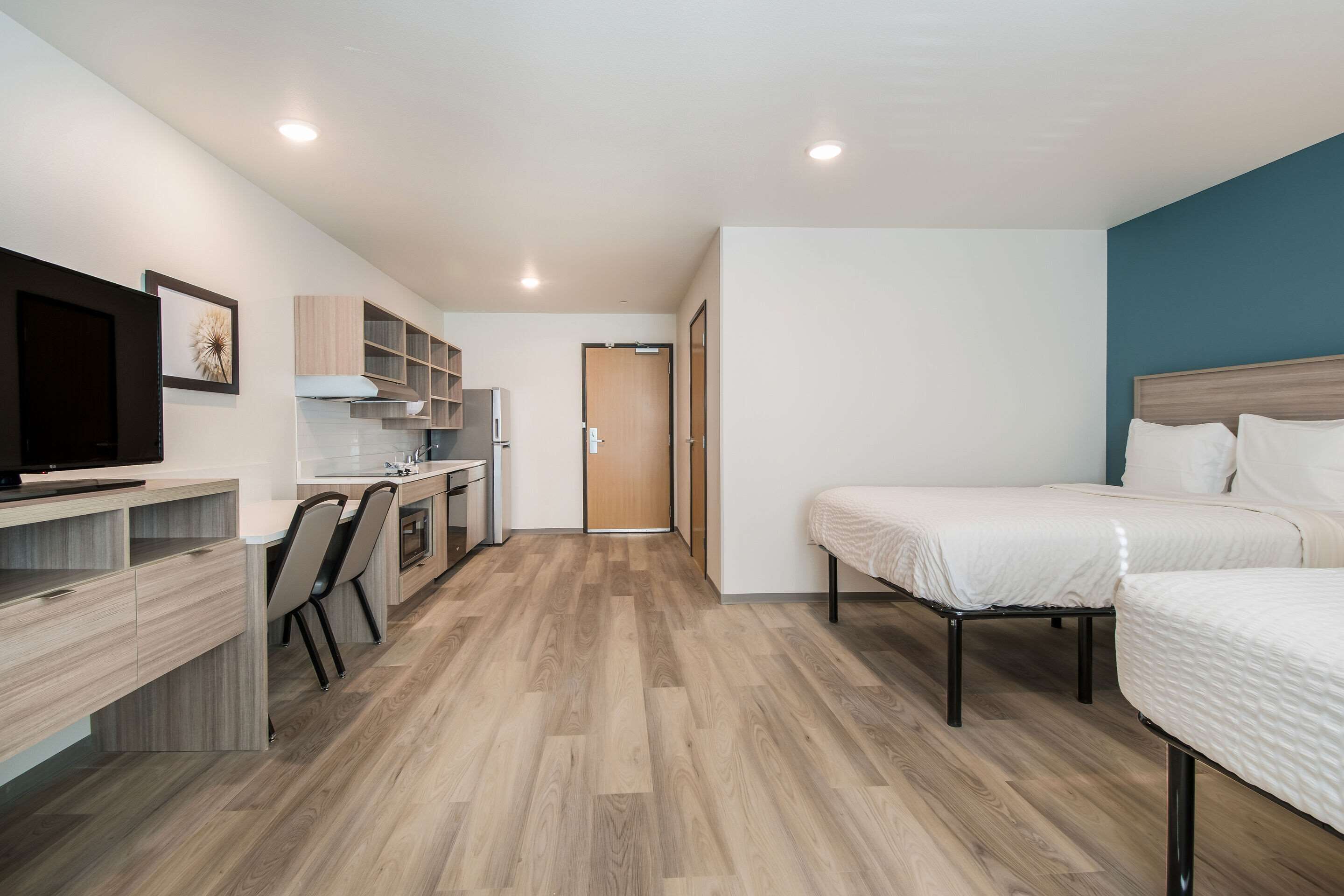 A modern hotel room with a kitchenette, a TV, a bed, and a bathroom.