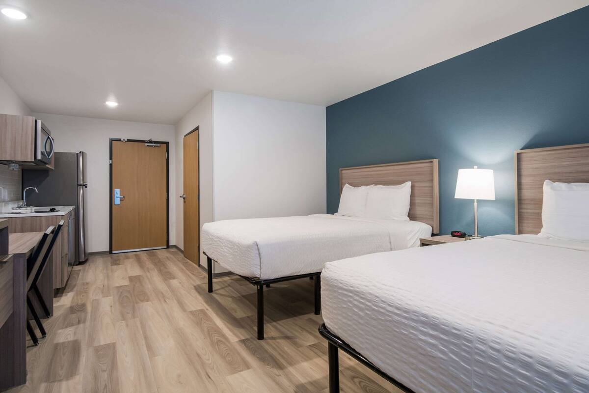 Hotellihuone, jossa on kaksi erillistä sänkyä, pieni keittiönurkkaus ja ovi, joka johtaa toiseen huoneeseen.