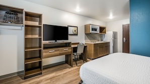 Quarto de hotel moderno com cama, escrivaninha com computador, televisão, micro-ondas e frigorífico.