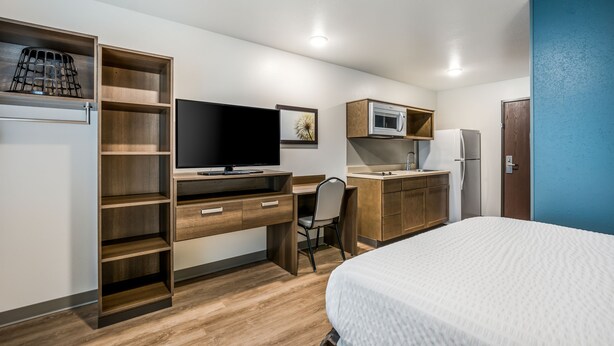 A modern hotel room with a bed, a desk with a computer, a TV, a microwave, and a refrigerator. - WoodSpring Suites Gurnee - Chicago (Gurnee)