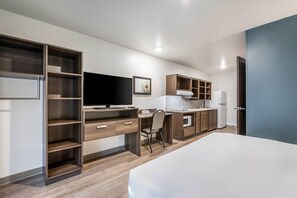 A modern bedroom with a large bed, a desk with a computer, a chair, and a wardrobe with multiple shelves. - WoodSpring Suites Gurnee - Chicago (Gurnee)