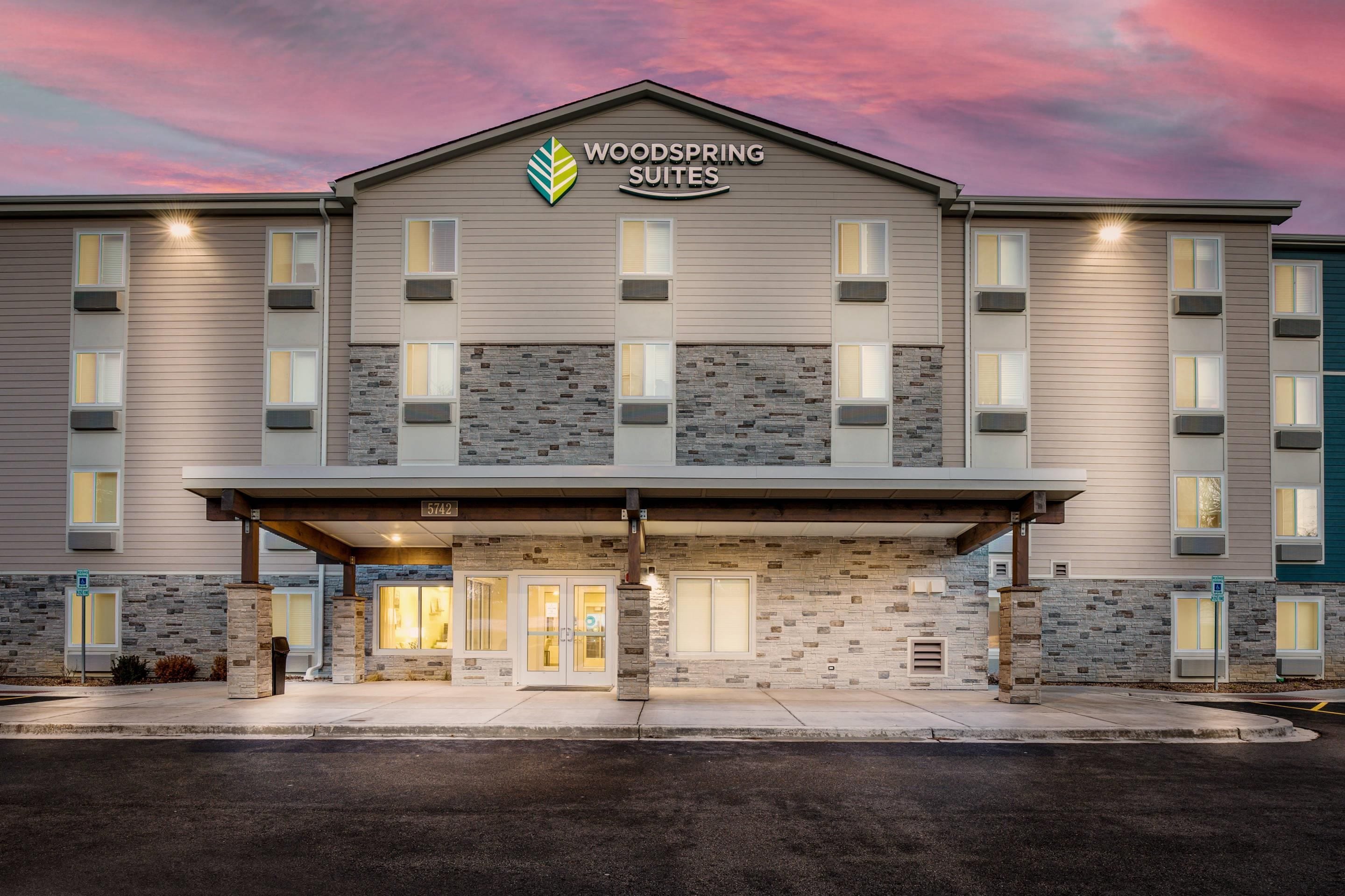 Un hotel de varios pisos con fachada de piedra, una entrada cubierta y un letrero que dice 'WOODS SPRING SUITES'.