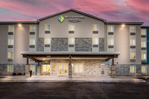 A multi-story hotel with a stone facade, a covered entrance, and a sign reading 'WOODS SPRING SUITES'. - WoodSpring Suites Gurnee - Chicago (Gurnee)