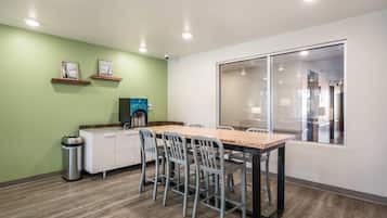 A modern kitchen with a dining area, equipped with a coffee machine, a trash bin, and a window with a view.