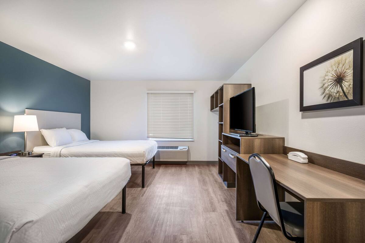 A hotel room with two beds, a desk, a chair, a TV, and a window with blinds.