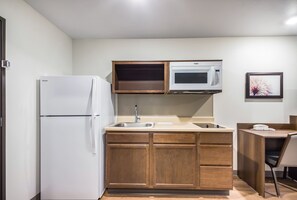 A compact kitchen with a refrigerator, microwave, sink, and wooden cabinets. - WoodSpring Suites Gurnee - Chicago (Gurnee)