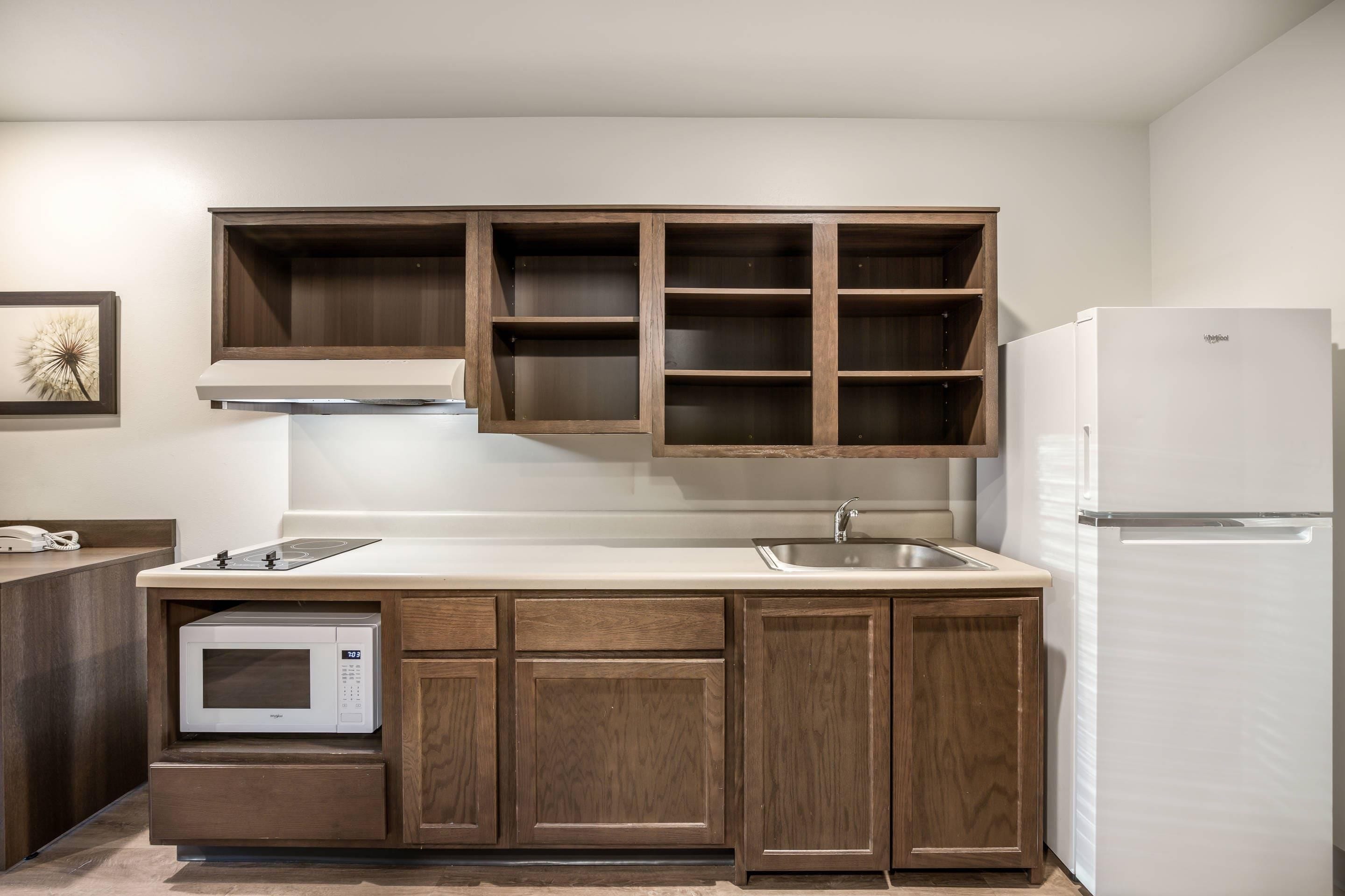 A kitchen with wooden cabinets, a built-in microwave, a stainless steel sink, and a white refrigerator.