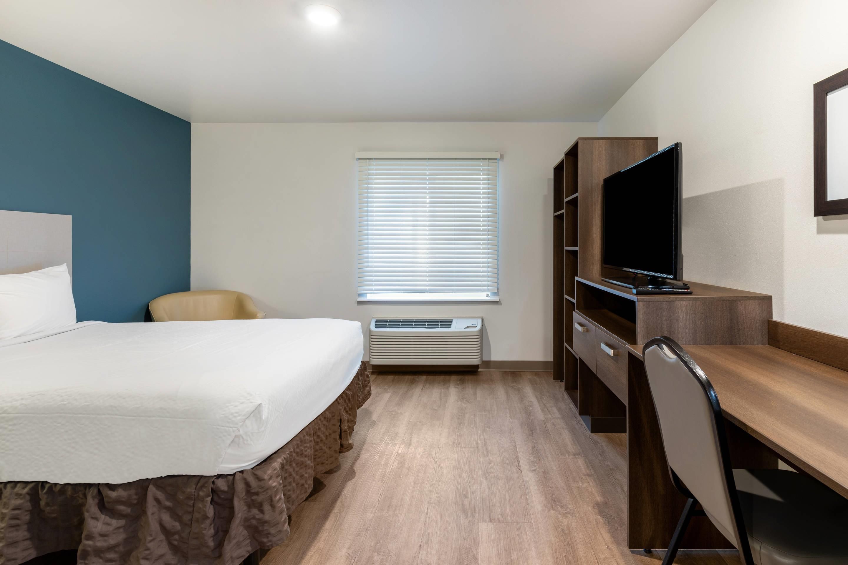 A hotel room with a bed, a desk, a chair, a television, and a window with blinds.