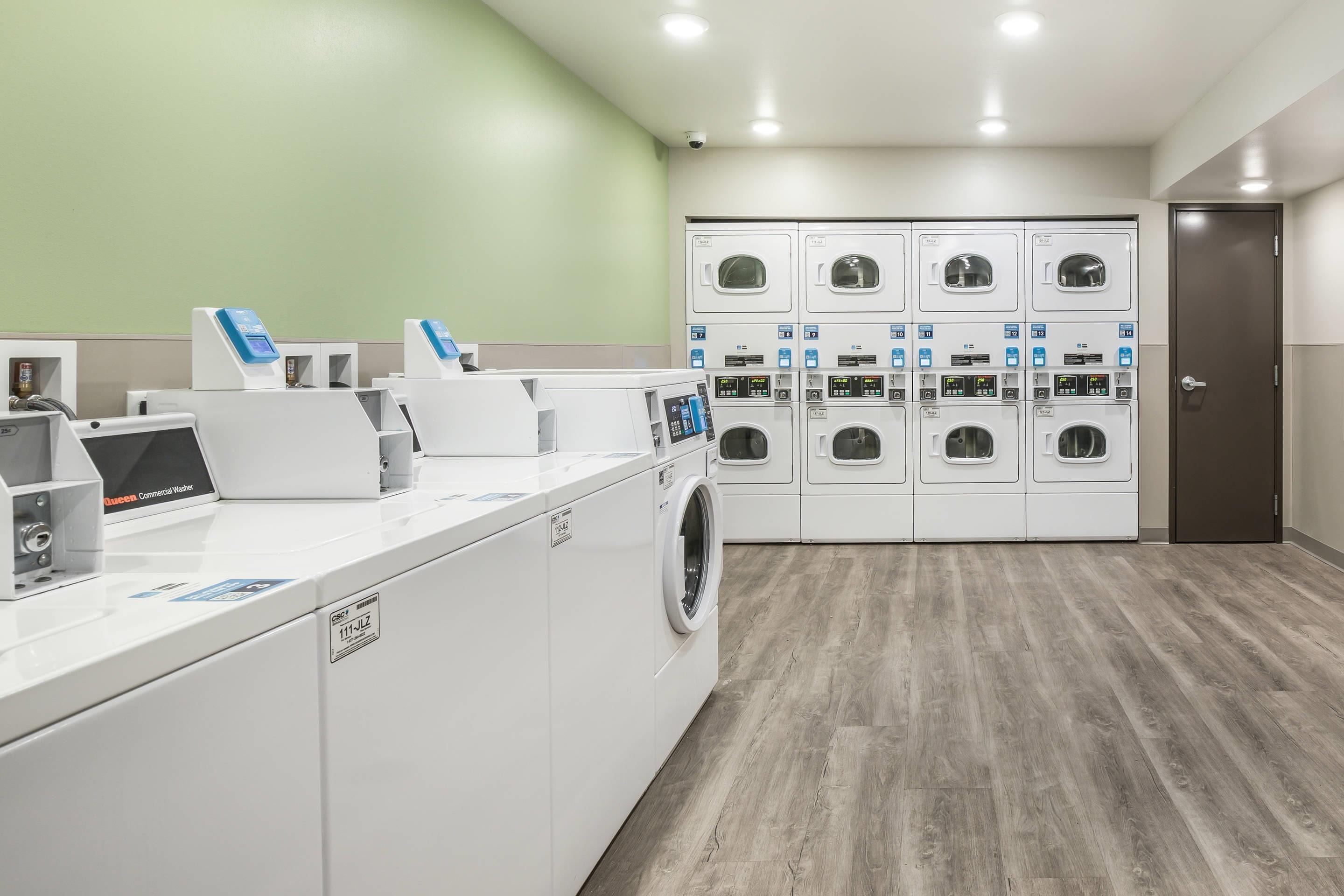 A laundry facility with multiple washing machines and dryers, a commercial washer, and a control panel.