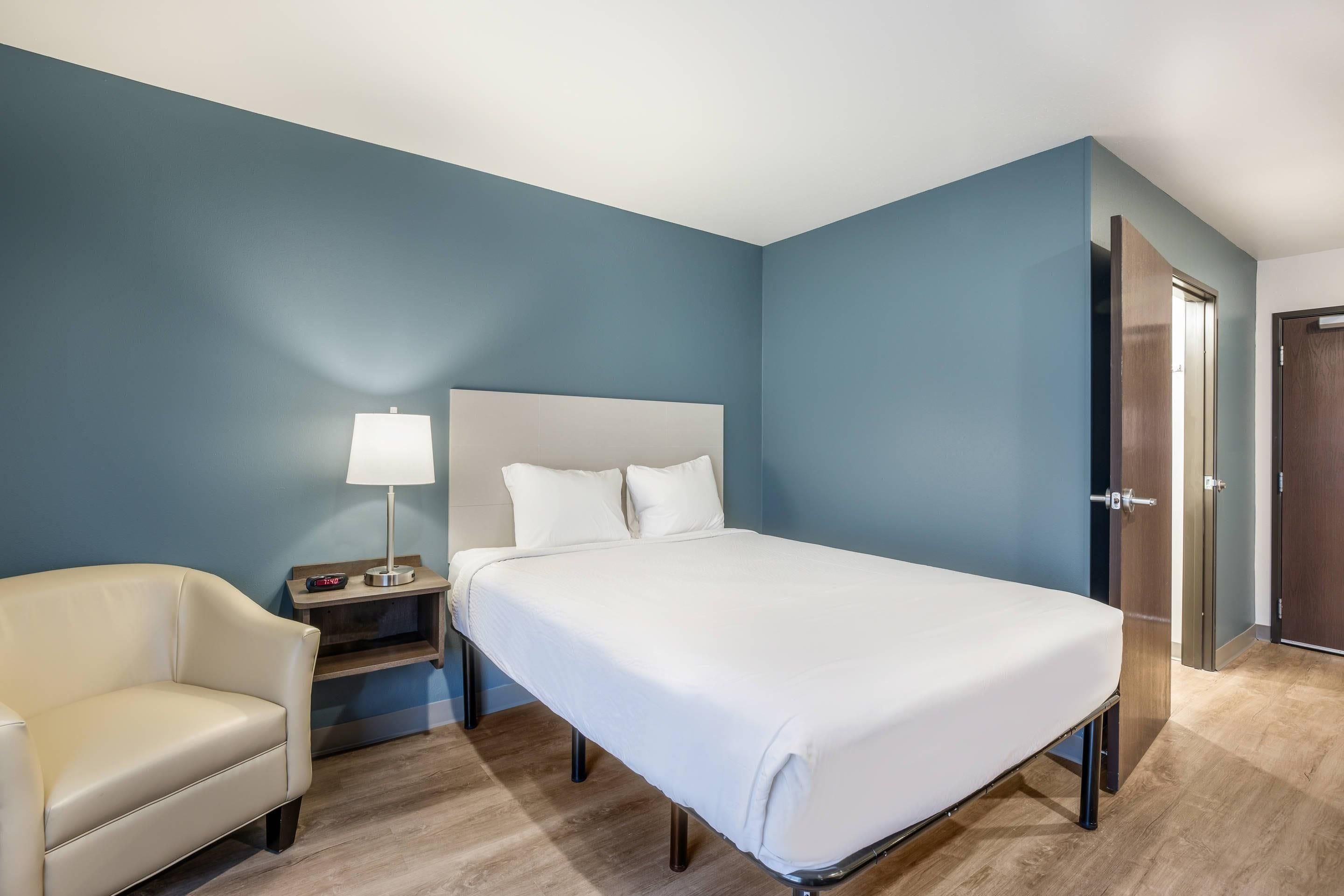 Une chambre d’hôtel comprenant un lit, une table de chevet, une lampe, une chaise et un plancher en bois.