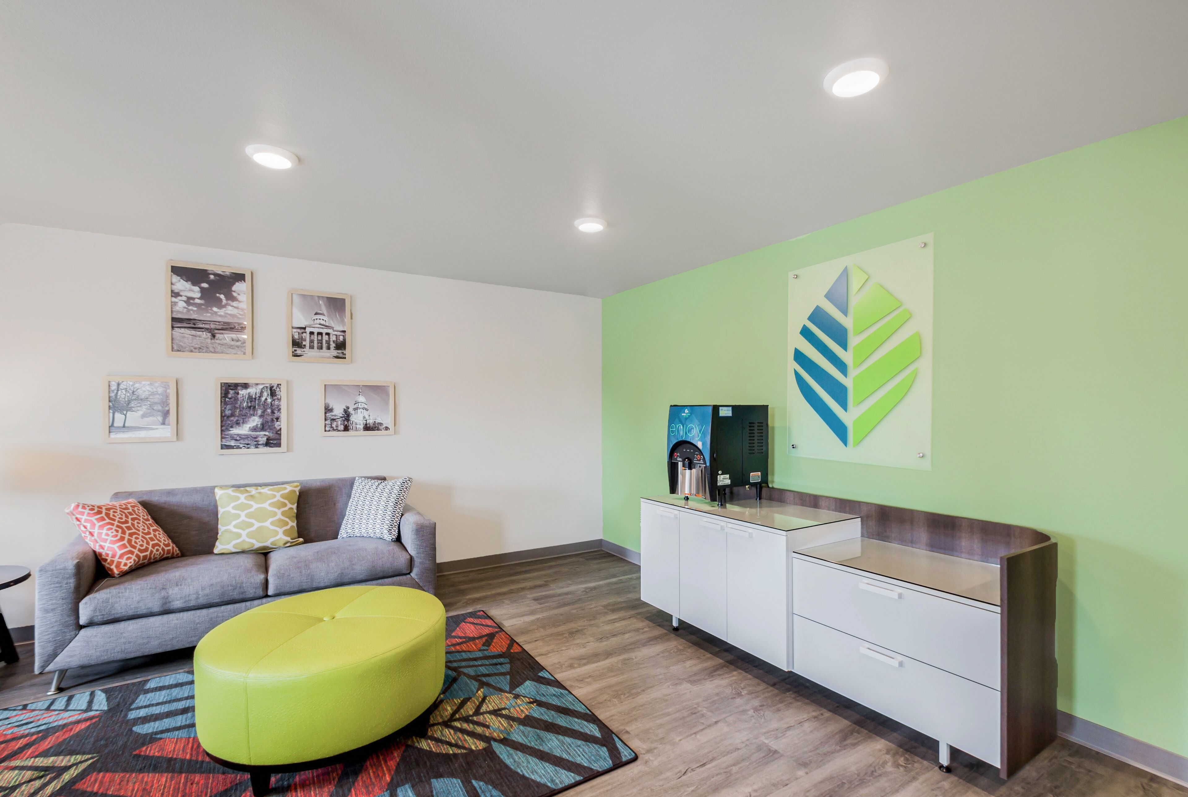 Una sala de estar moderna con un sofá gris, cojines coloridos, un reposapiés verde y una alfombra estampada.