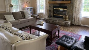 A living room with a stone fireplace, a sofa, a coffee table, and a black leather ottoman.