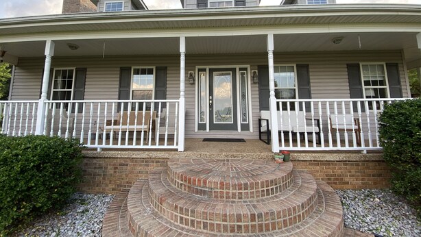 A two-story house with a covered porch, a brick staircase, and a front door with a decorative glass panel.