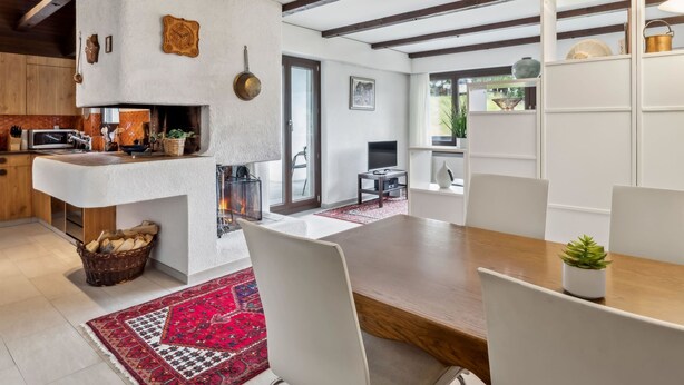 Een moderne keuken met een ingebouwde open haard, houten balken en een eethoek met een rood tapijt.