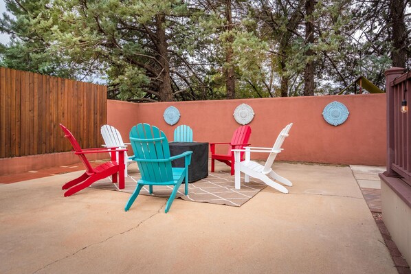 Une terrasse extérieure avec des fauteuils Adirondack de couleur rouge, turquoise et blanche, une table noire et des décorations murales.