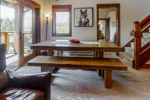 Cozy room with a dining table, comfortable chair, and framed picture, featuring a staircase and large window.